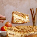 A hand holds a piece of apple cheesecake on a pie server.
