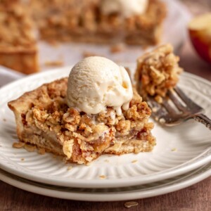 A slice of apple crumble tart on a plate with a fork next to it and ice cream on top.