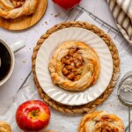 Apple danish on a plate with other pastries scattered around.