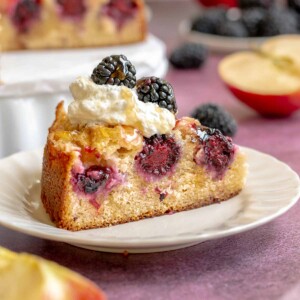 A slice of blackberry apple cake on a plate with whipped cream on top.
