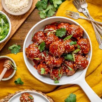 A bowl of honey sriracha meatballs with garnishes surrounding the bowl.