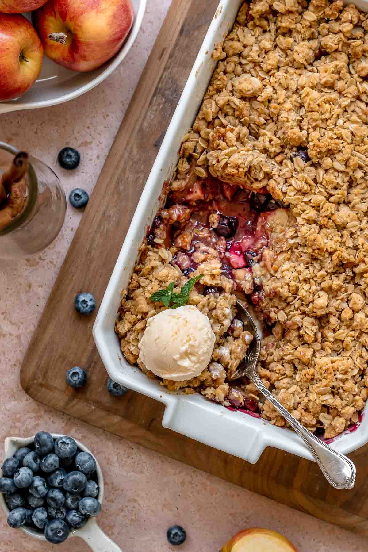 Apple blueberry crisp in a casserole dish with a scoop removed and vanilla ice cream on top.