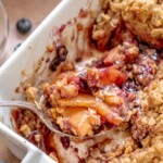 A scoop of apple blueberry crisp on a spoon sitting in a casserole dish.