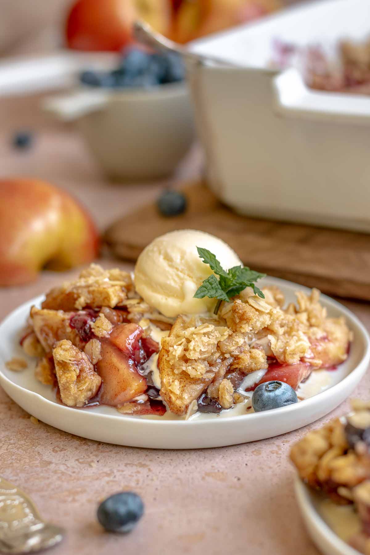 Apple blueberry crisp on a plate with a scoop of ice cream on top.
