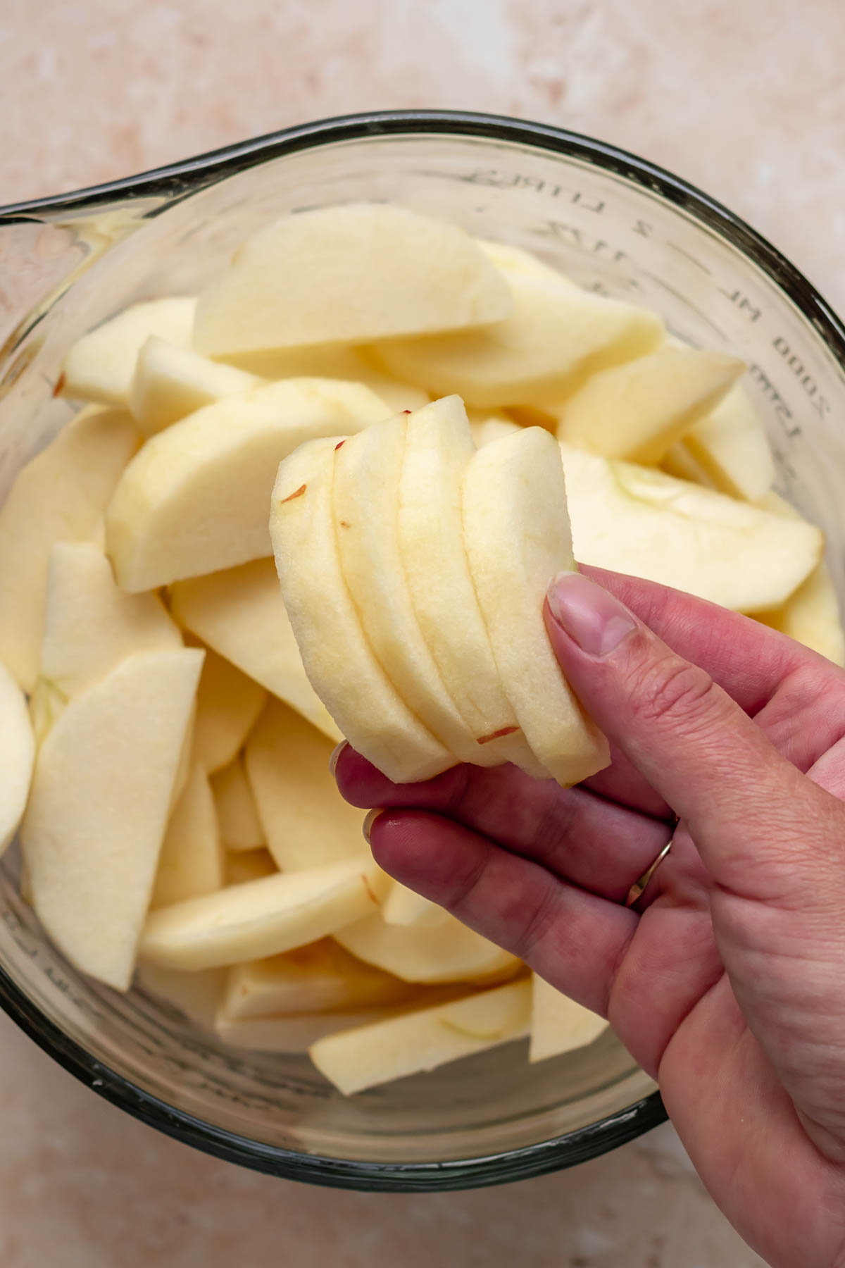 A hand holds sliced apples over a bowl.