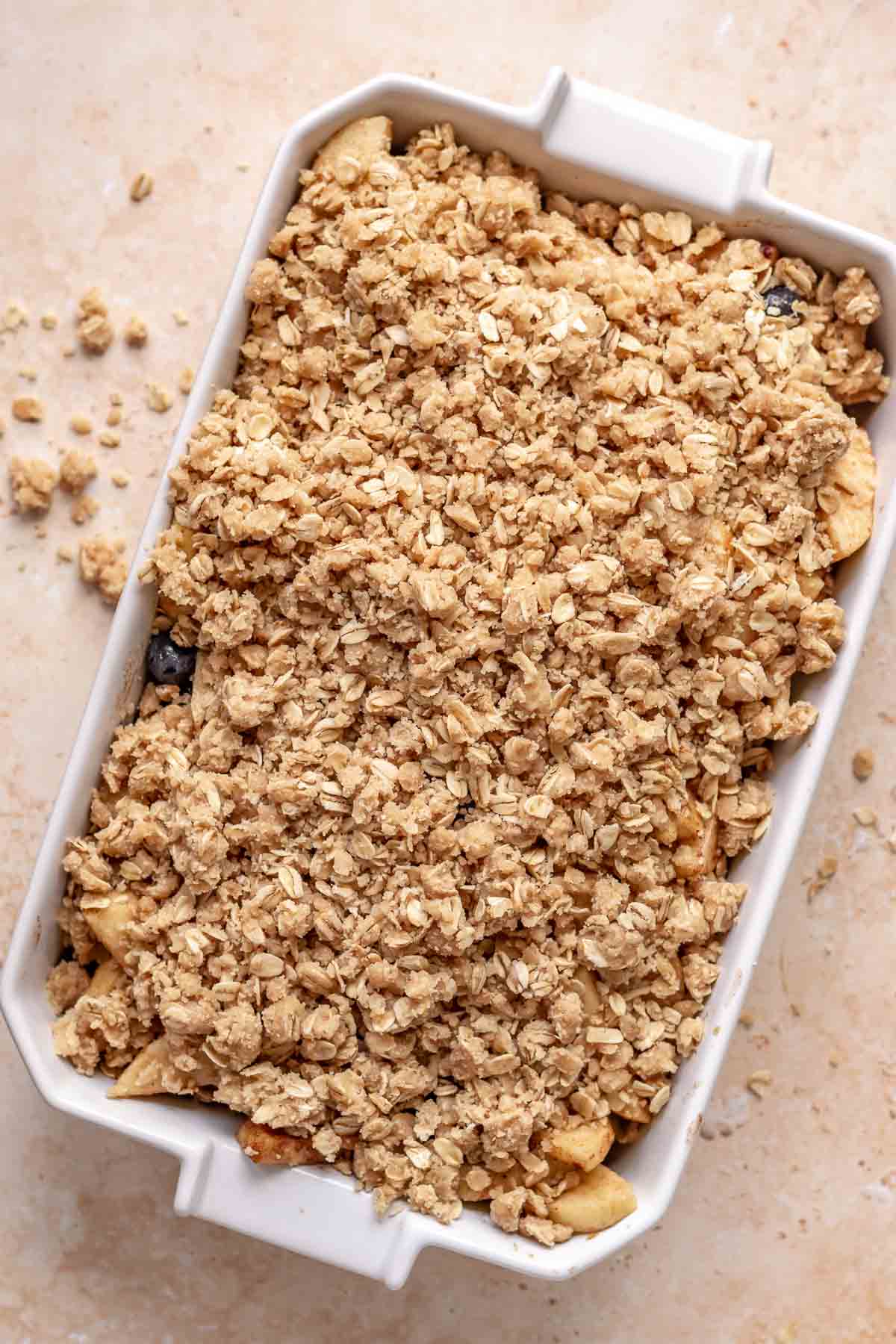 Crisp topping on top of apples and blueberries in a casserole dish before baking.