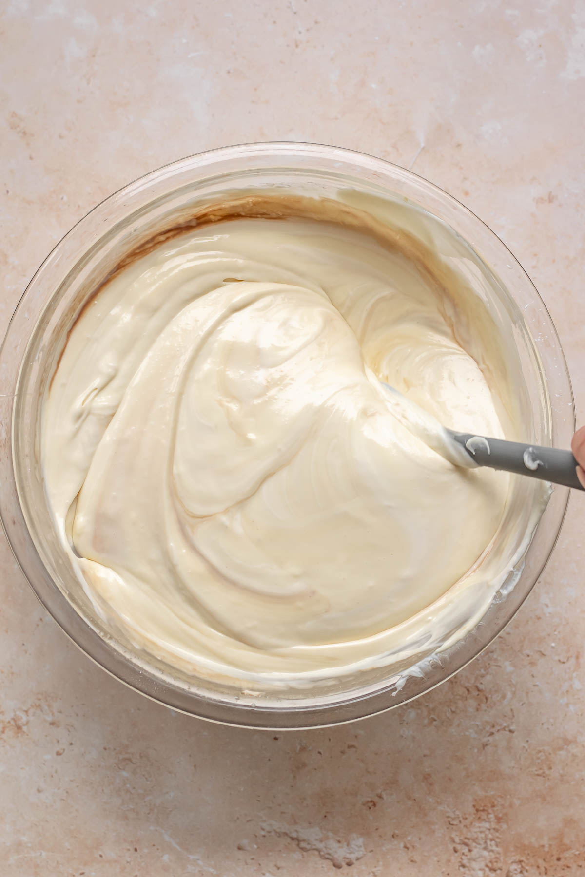 A spatula folds sour cream and vanilla into cheesecake batter.