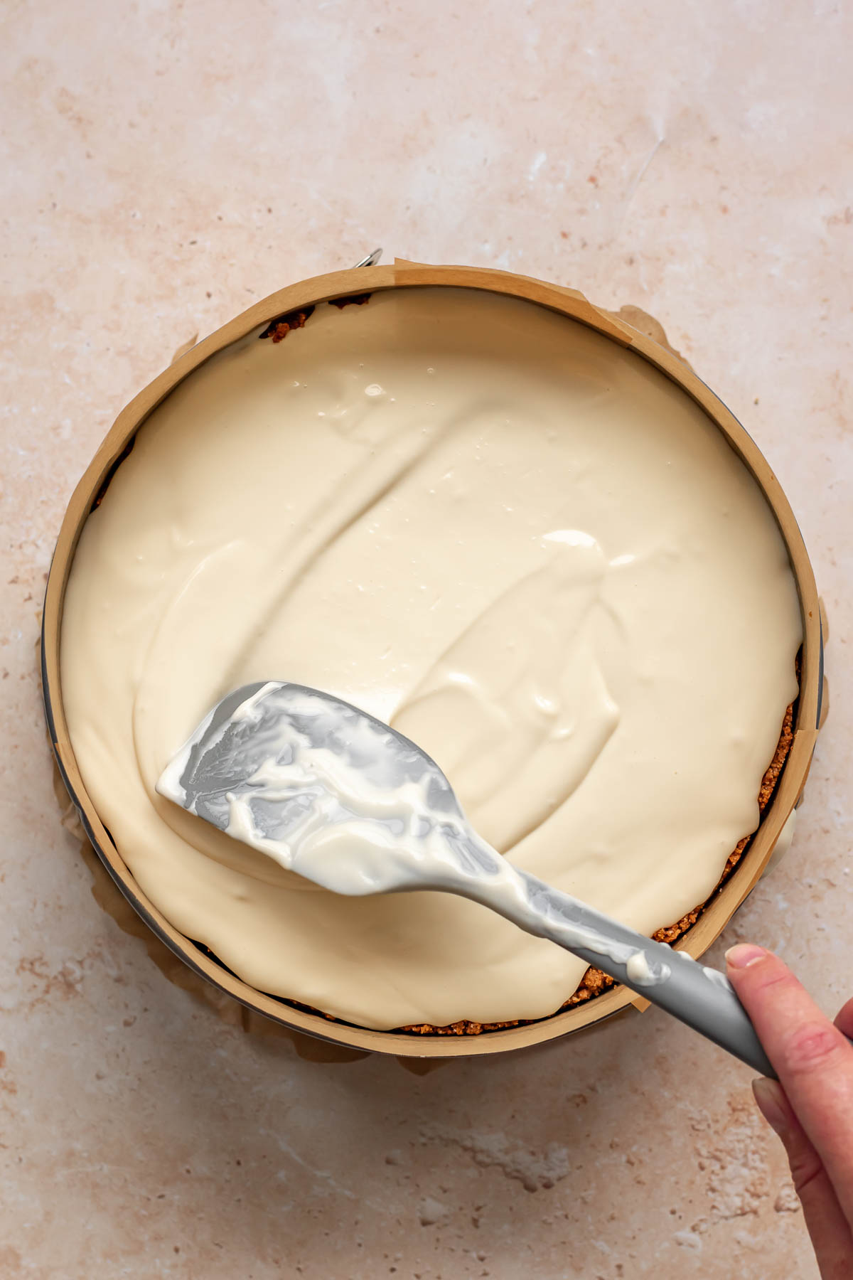 A spatula spreads cheesecake batter evenly.