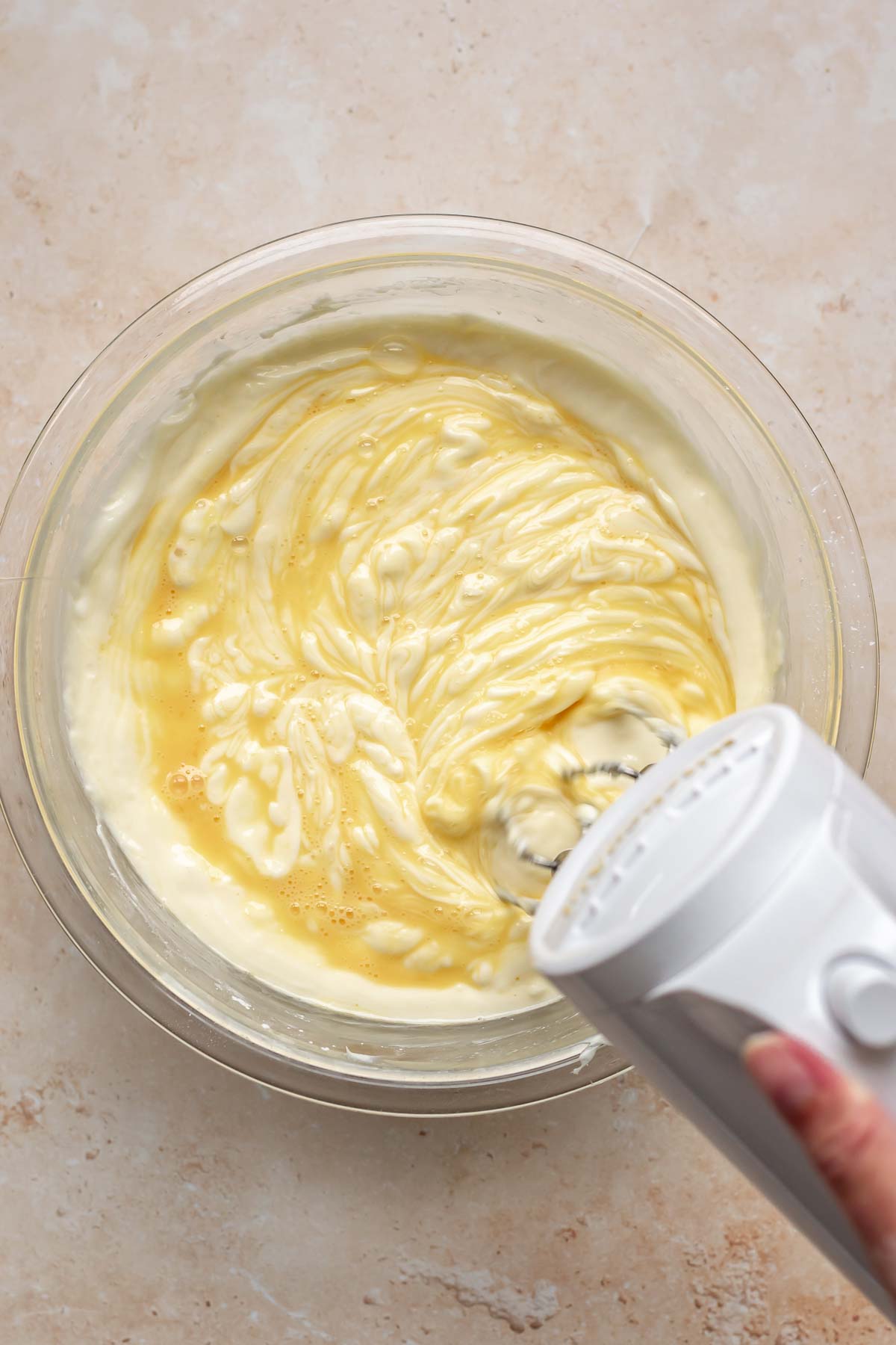 A mixer beats whisked eggs into cheesecake batter.