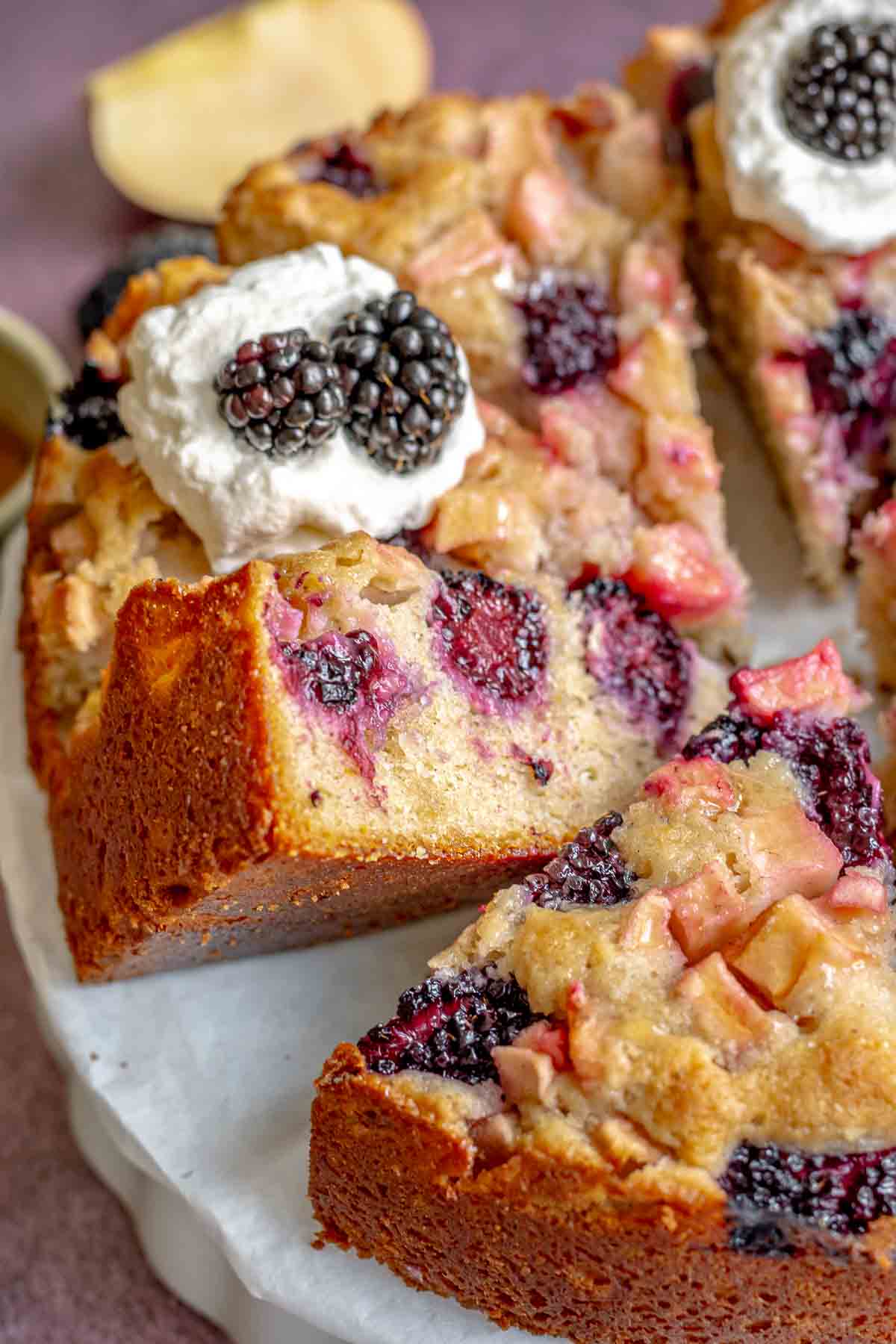 Sliced apple blackberry cake on a platter with one piece laying on its side.