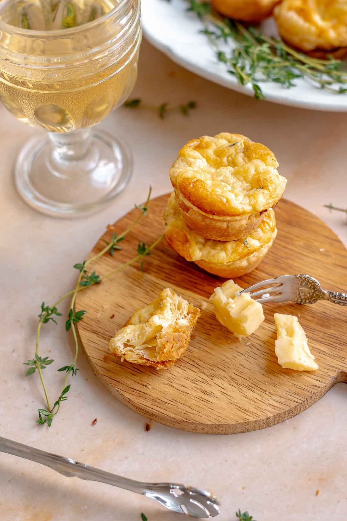 A stack of cheese puffs on a wooden board with pieces of cheese next to it.