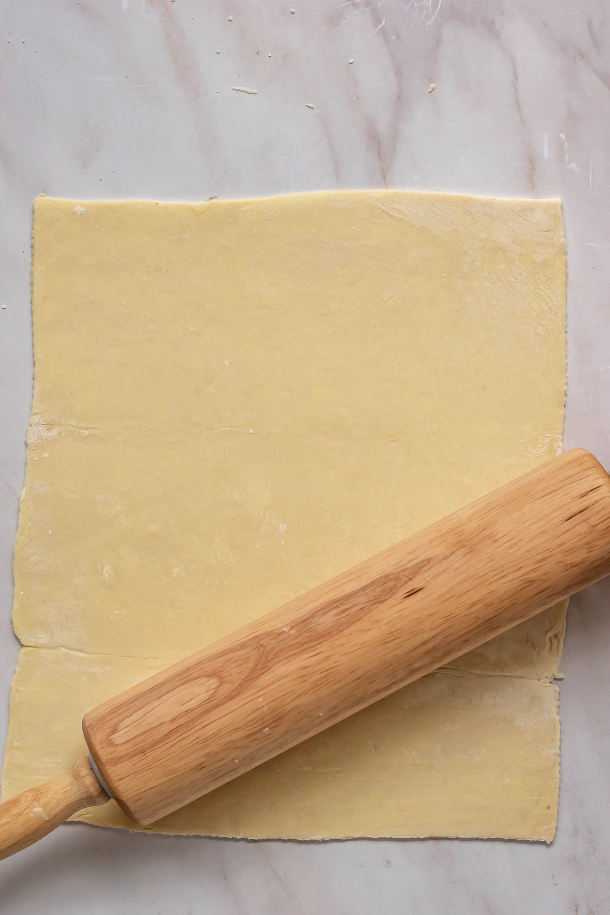 A rolling pins rolls out puff pastry.