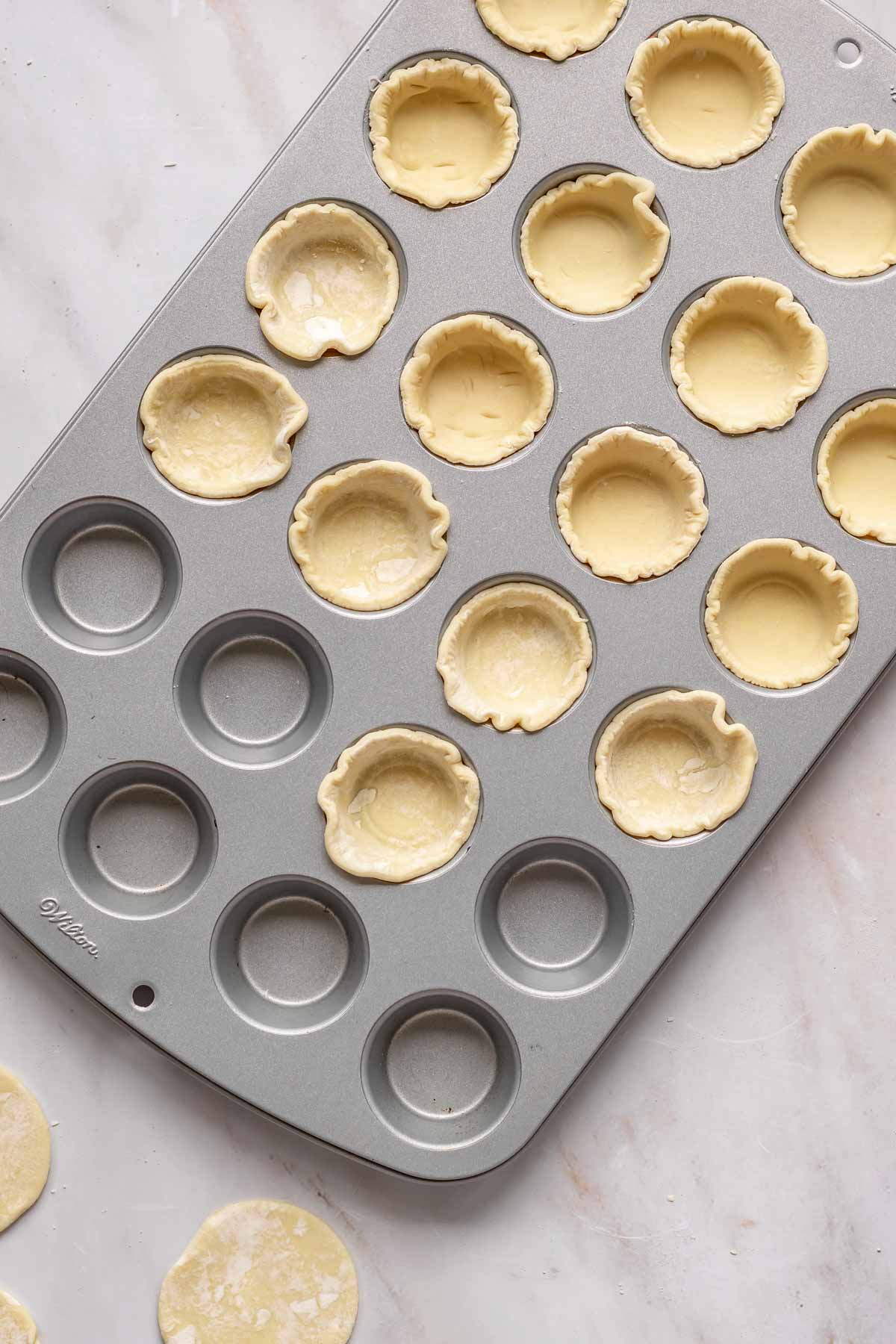 Puff pastry rounds pressed into a mini muffin tin.