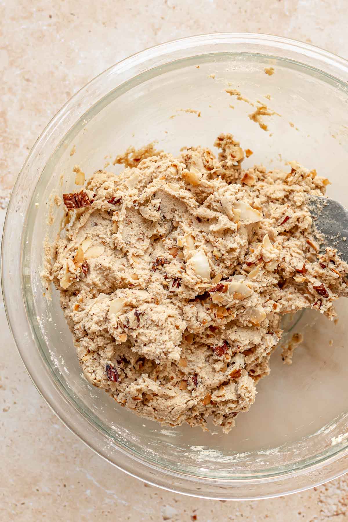A spatula folds pecans and coconut into cookie dough.