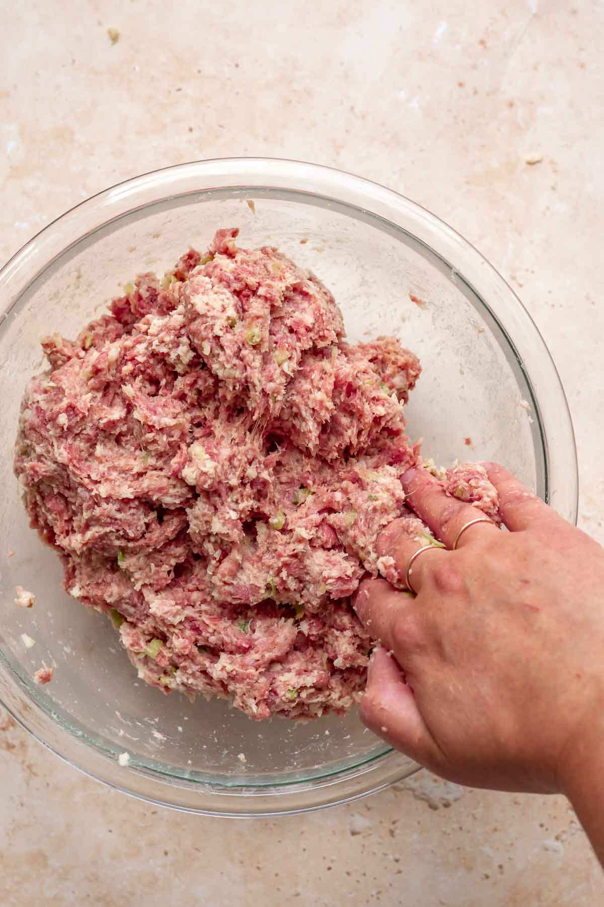 A hand mixes soaked breadcrumbs into meatball mixture.