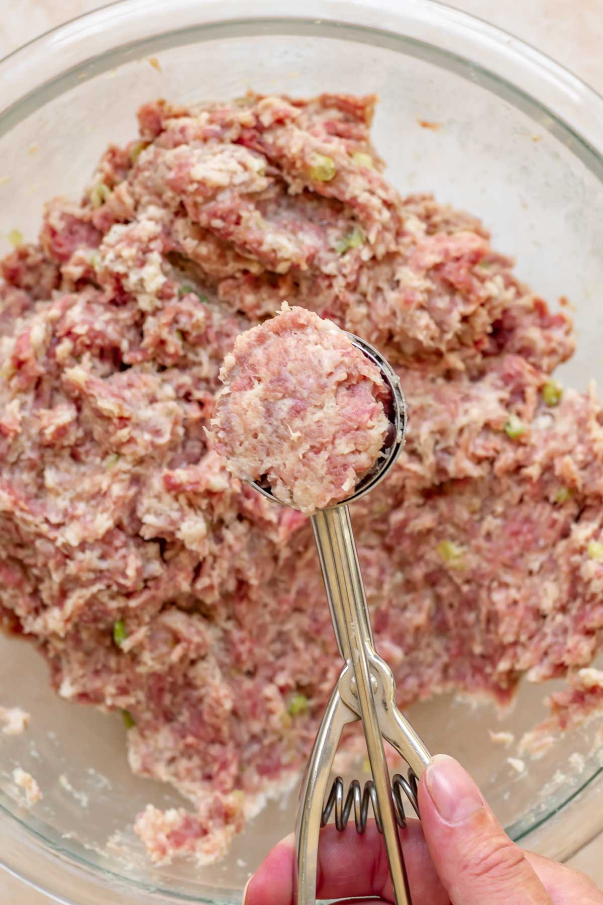 A cookie scoop holds a flush scoop of raw meatball meat.