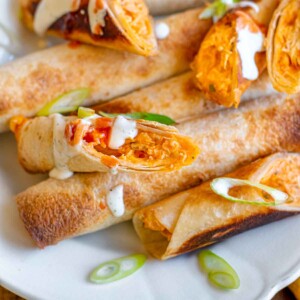 Buffalo chicken taquitos on a platter drizzled with ranch.