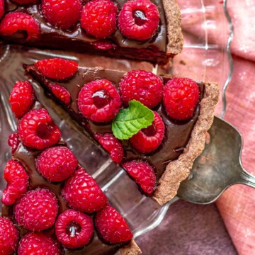 A serving utensil removes a slice of chocolate raspberry tart from a platter.