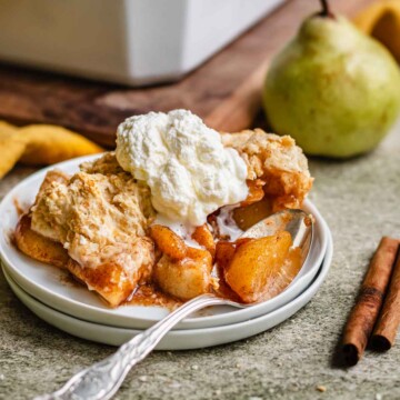 Pear cobbler on a plate topped with whipped cream.