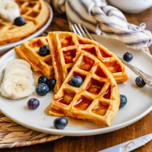 Triangles of sweet potato waffles on a plate with syrup and fruit.