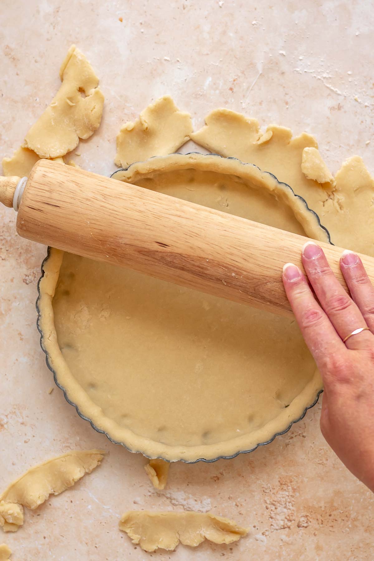 A rolling pin goes over the top of a tart pan to remove excess pastry.
