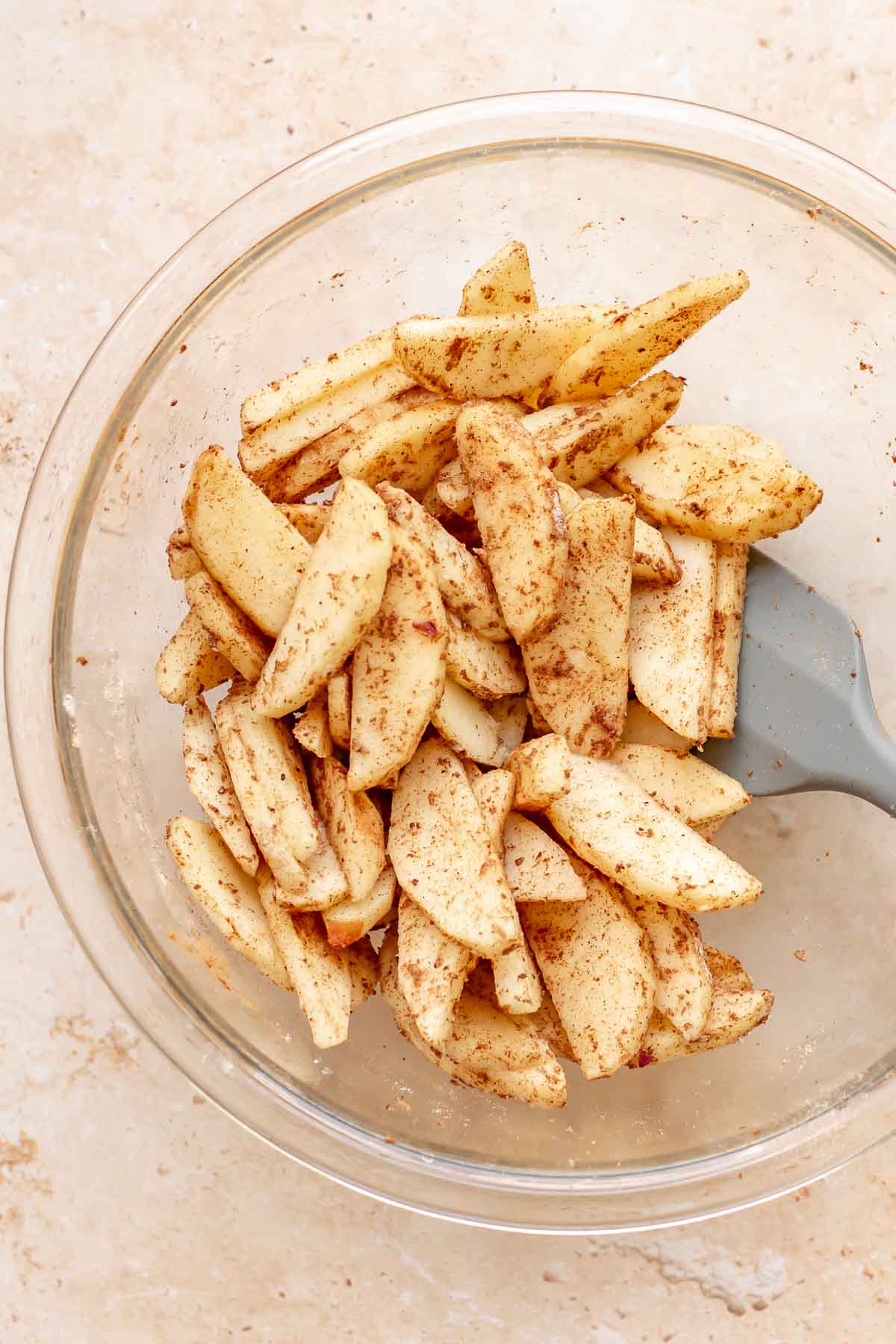 A spatula mixes apple slices and spices in a bowl.