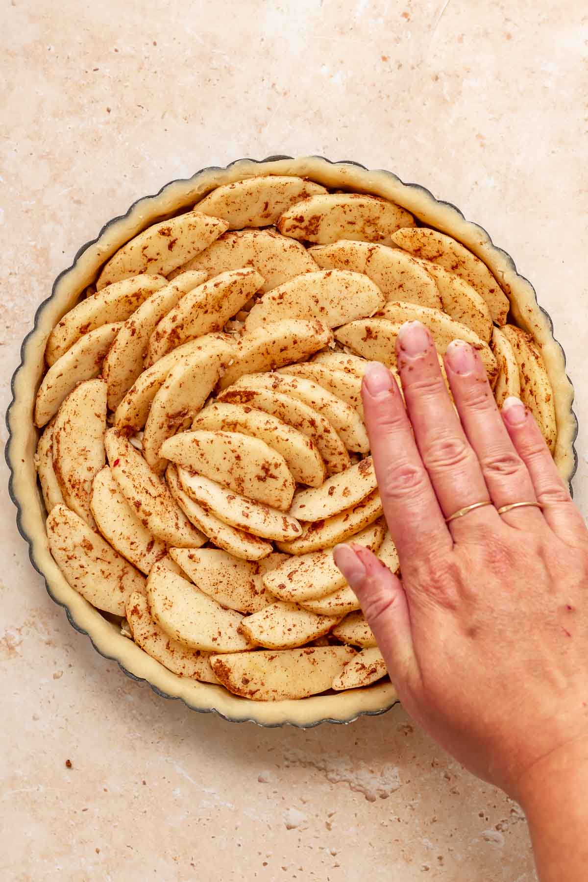 A hand pressed down on apples spiraled in a tart pan.