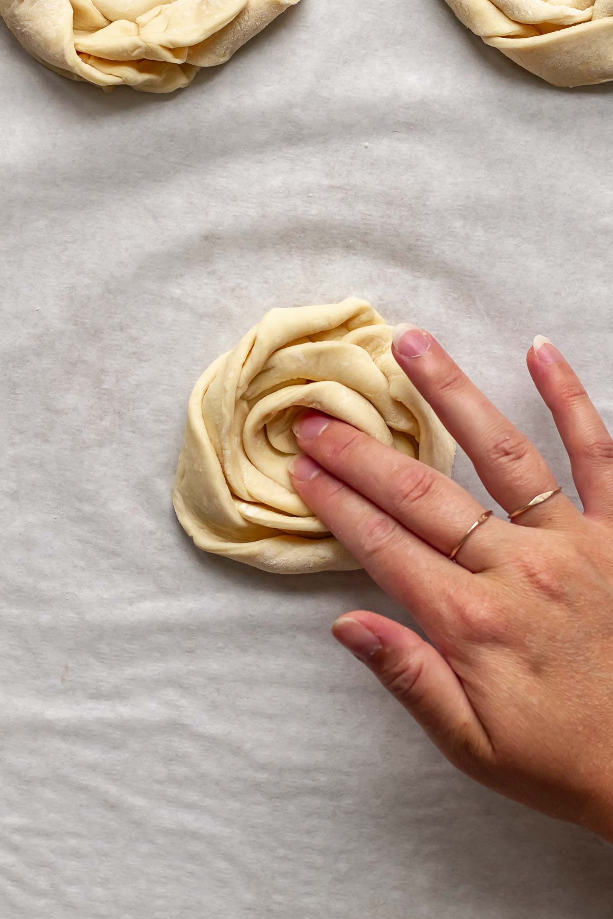 A hand presses down the middle of the puff pastry coil.