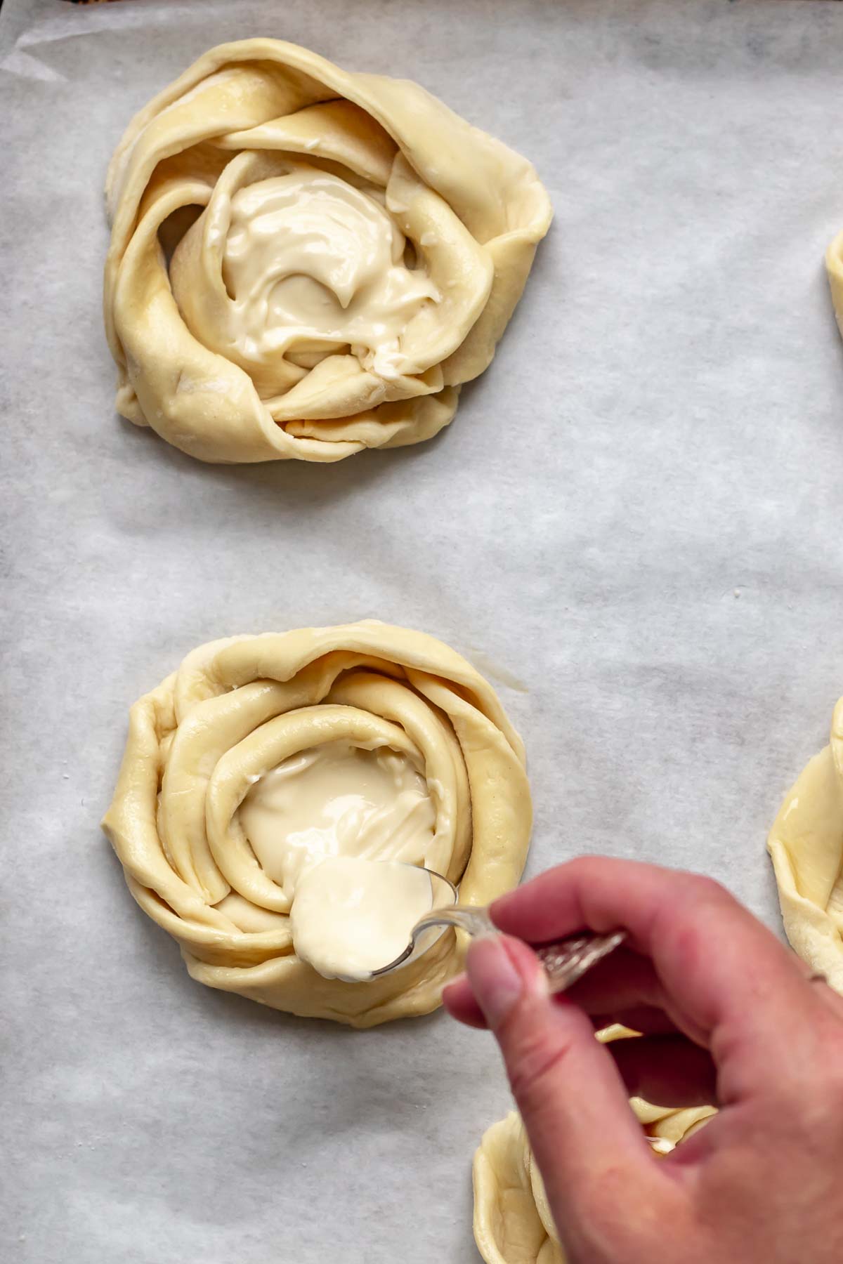 A hand adds cream cheese mixture to the center of the puff pastry roses.