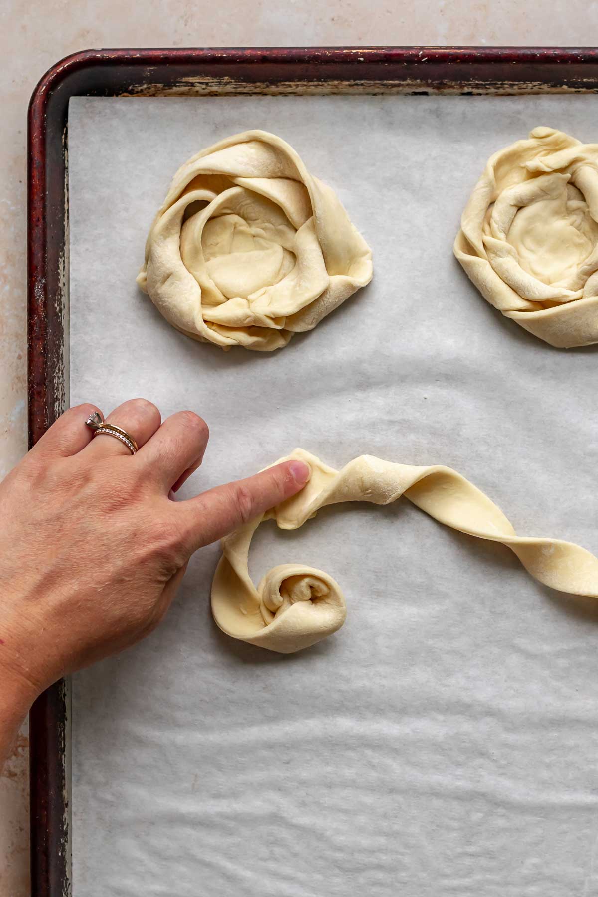 A hand presses together two strips of coiled puff pastry.