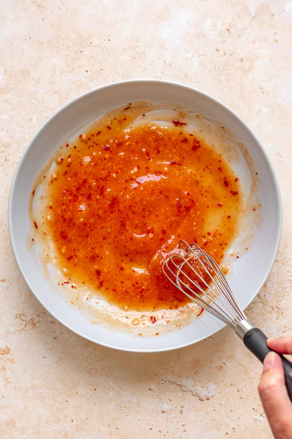 A hand whisks together sweet chili sauce in a bowl.