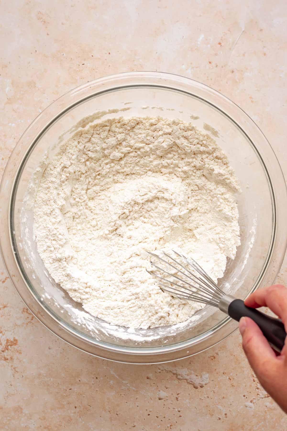 A hand whisks together dry ingredients in a bowl.