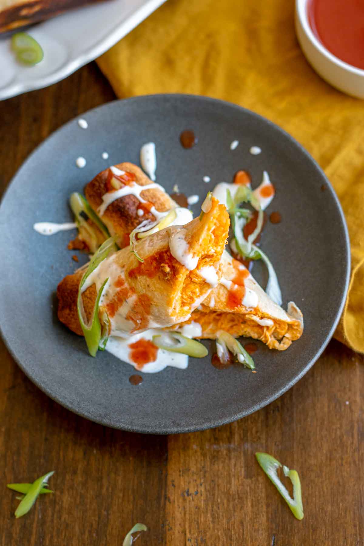 Buffalo chicken taquito split in half on a plate, drizzled with ranch and buffalo sauce.