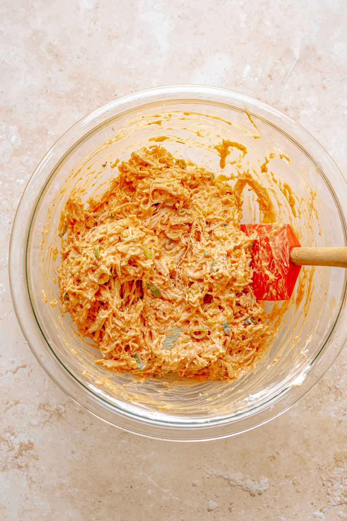 A rubber spatula folds together buffalo chicken taquito ingredients in a bowl.