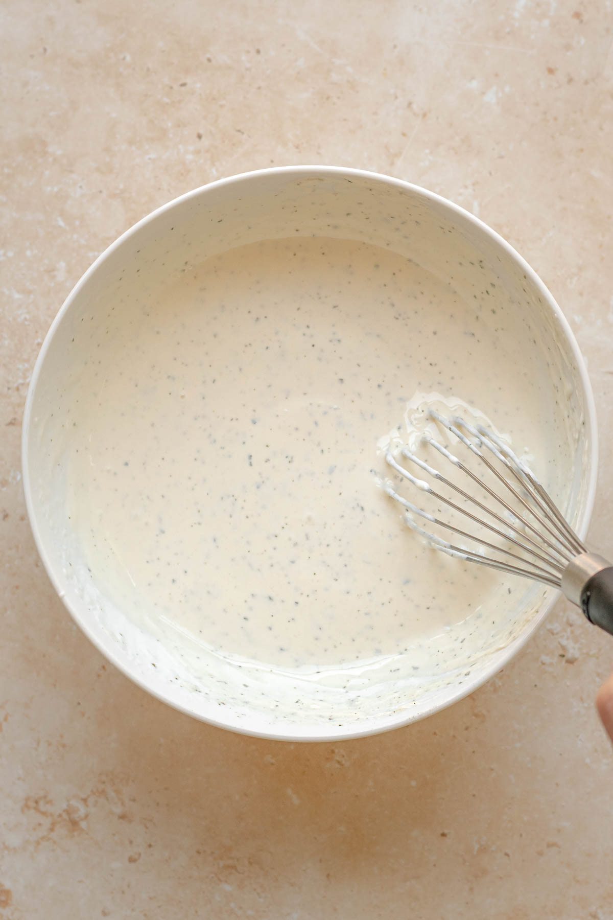 A whisk mixes ranch dip in a bowl.