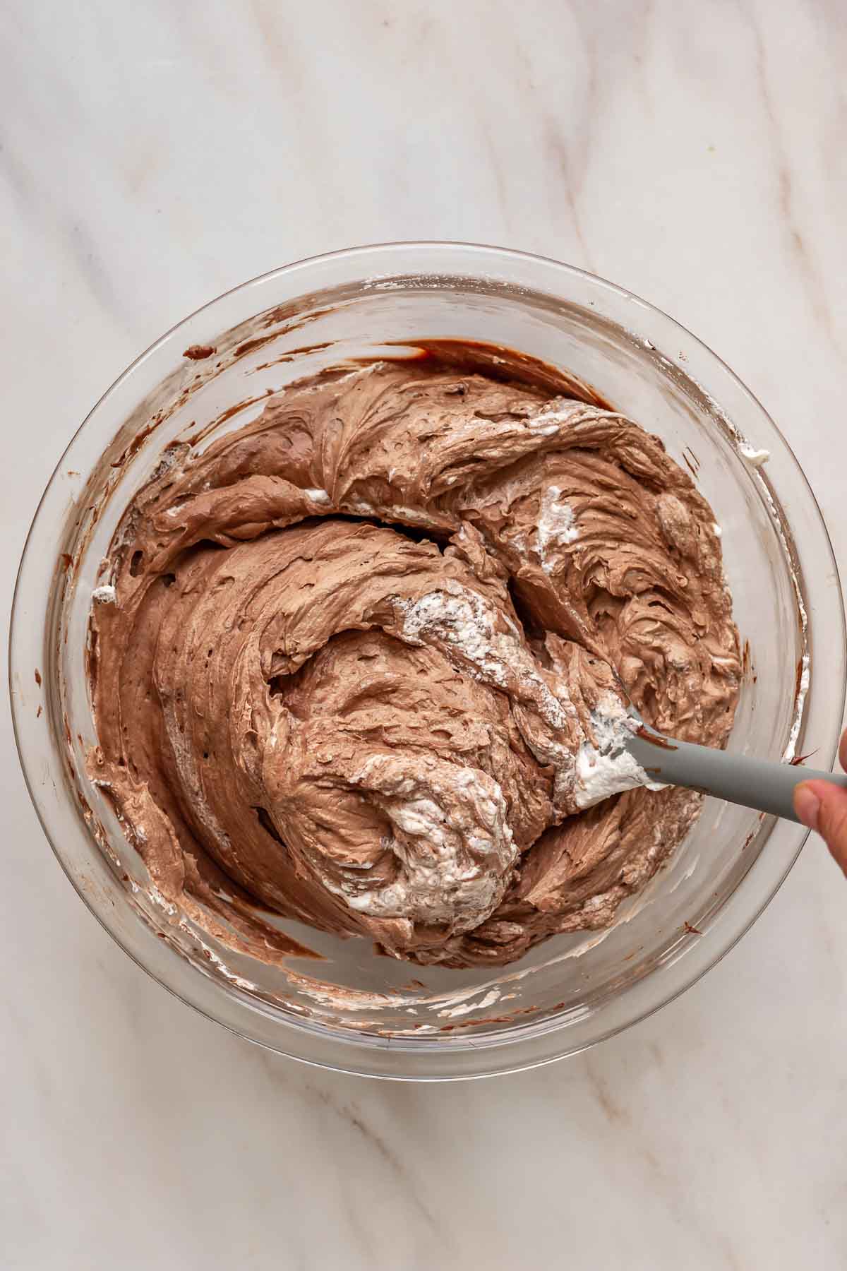 A rubber spatula folds whipped cream into chocolate cheesecake batter.