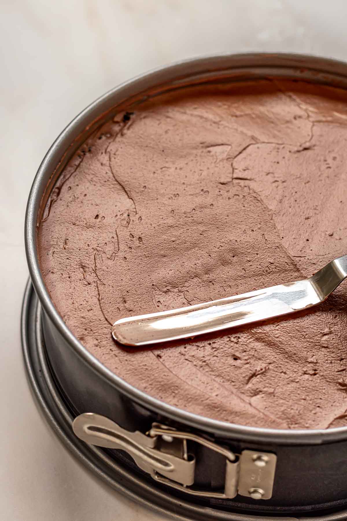An offset spatula smooths chocolate orange cheesecake batter into a springform pan.