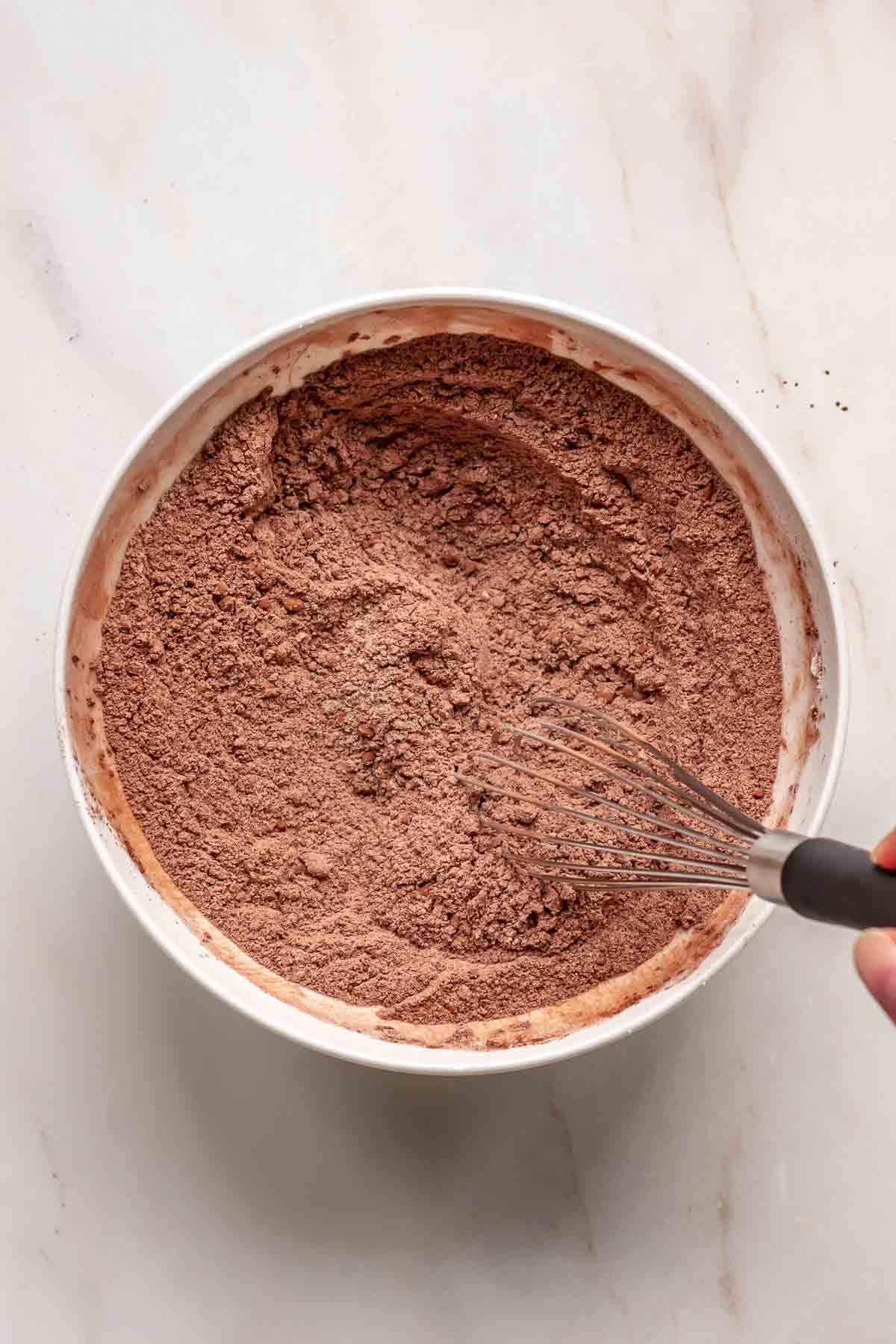 A hand whisks together dry ingredients and cocoa powder.