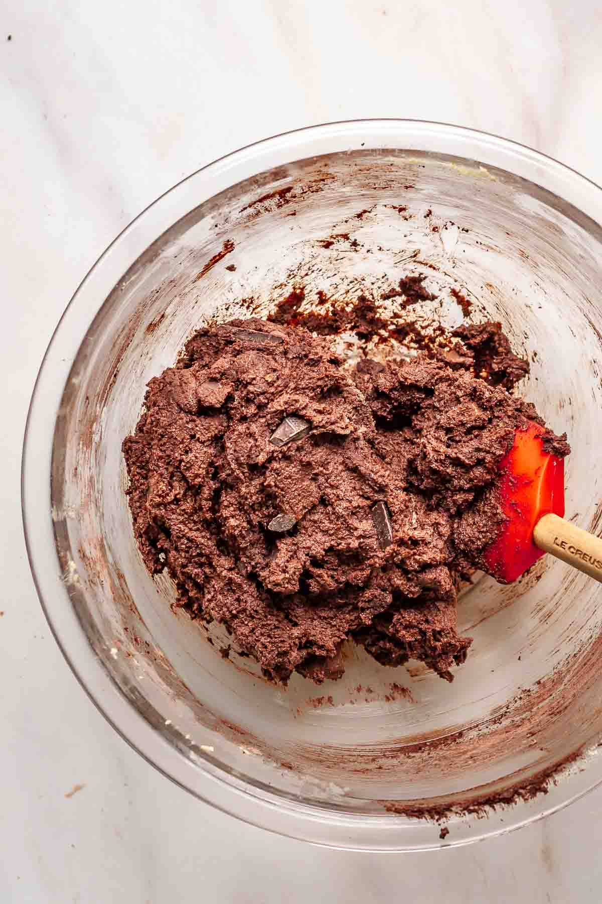 A rubber spatula folds together chocolate orange cookie dough in a bowl.