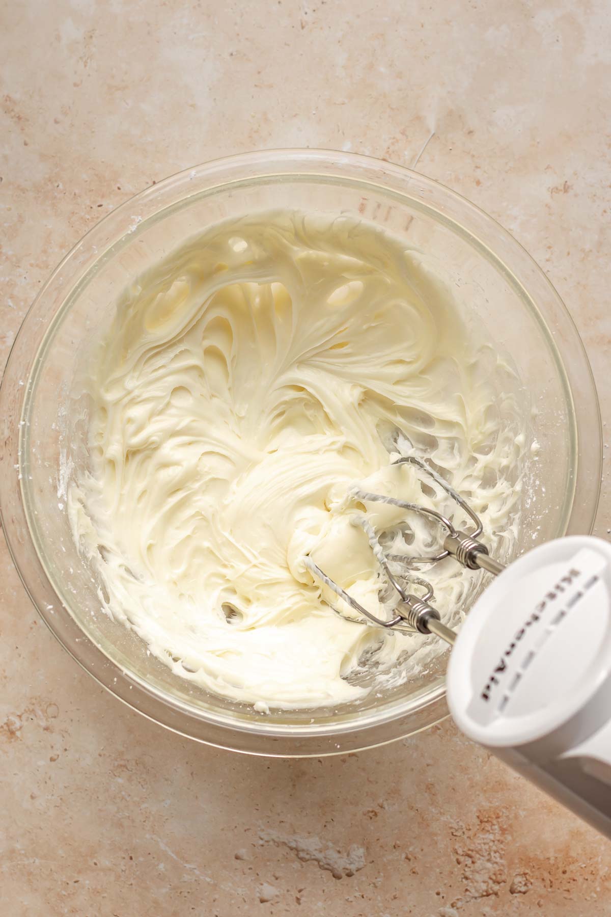 A hand mixer mixes cream cheese and sugar in a bowl.