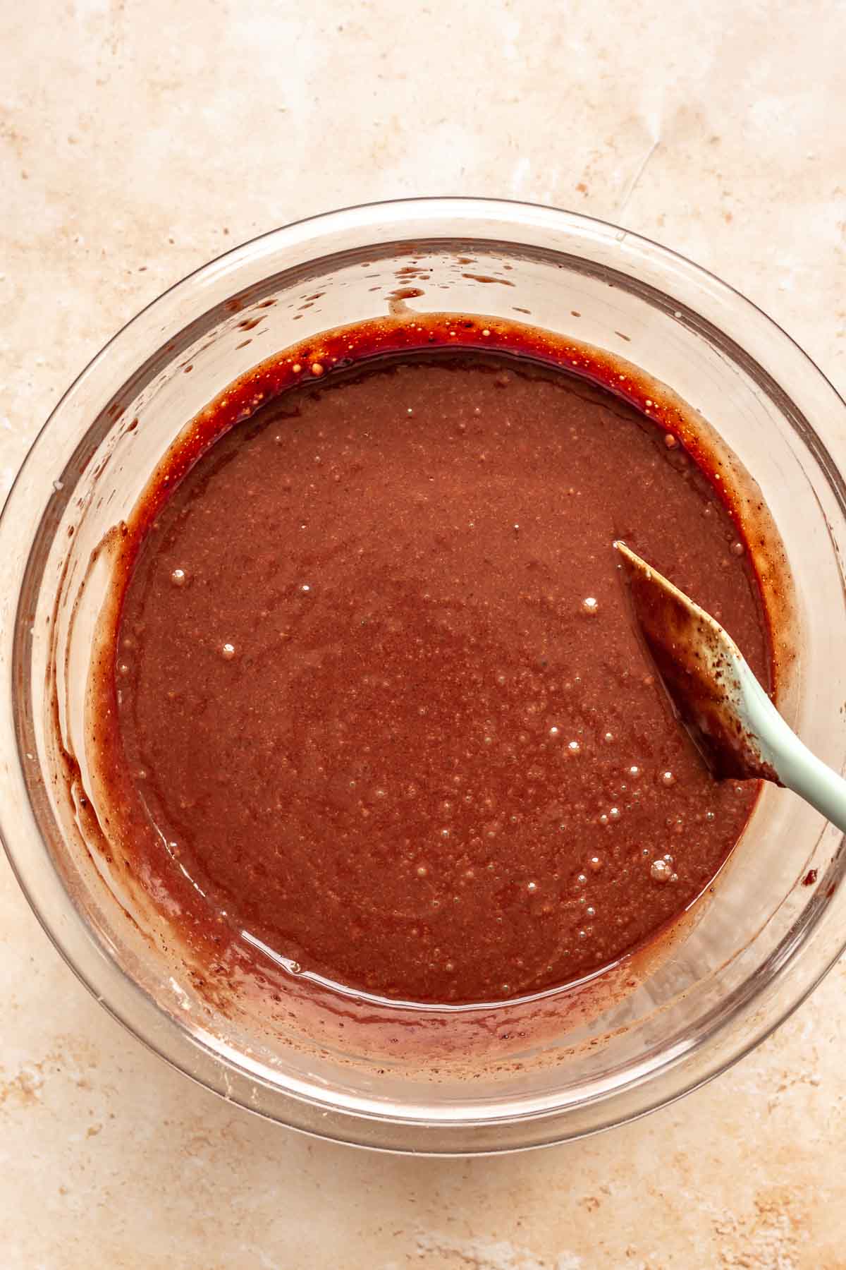 Thin chocolate cake batter being stirred with a rubber spatula.