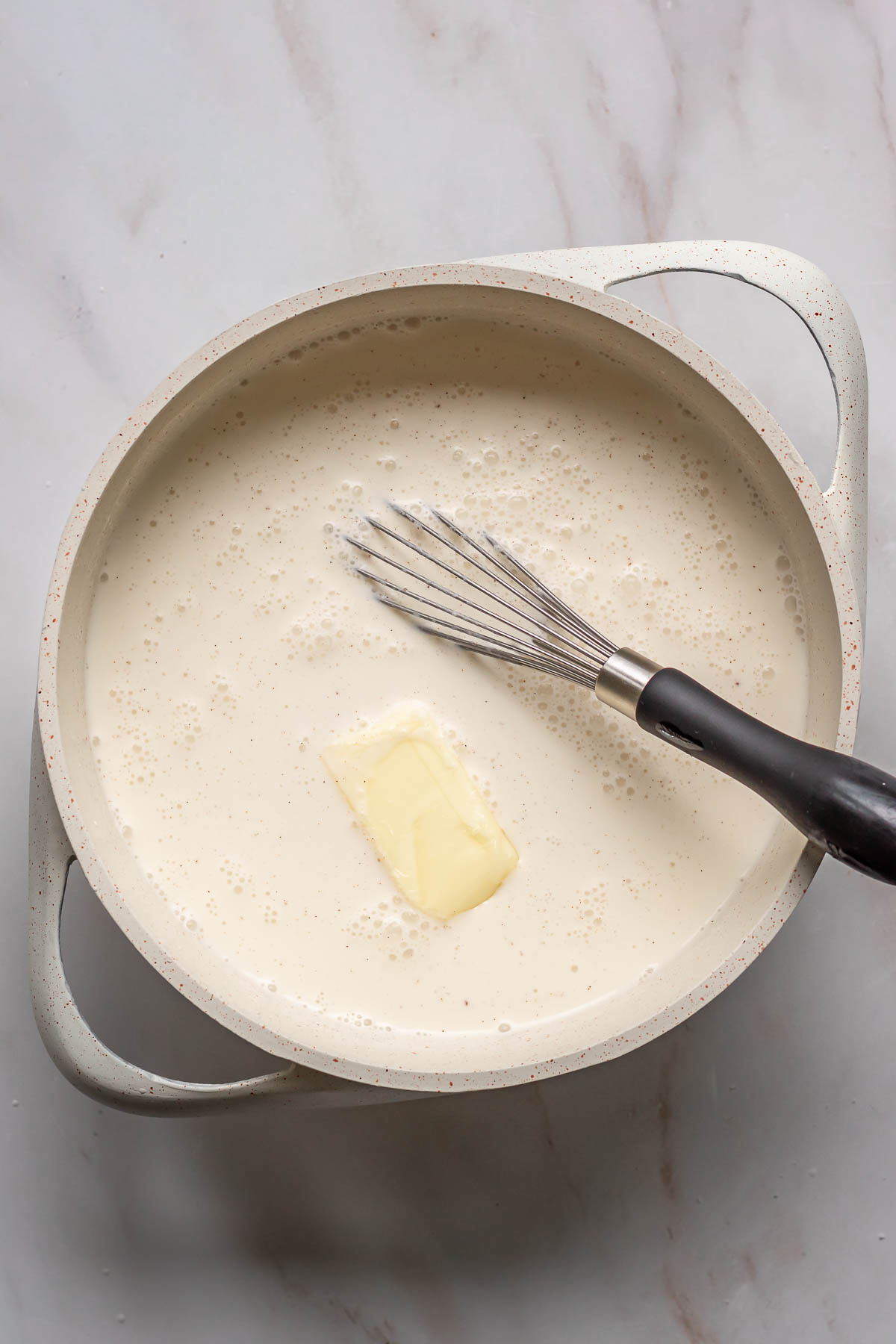 Heavy cream, milk and butter being whisked in a saucepan.