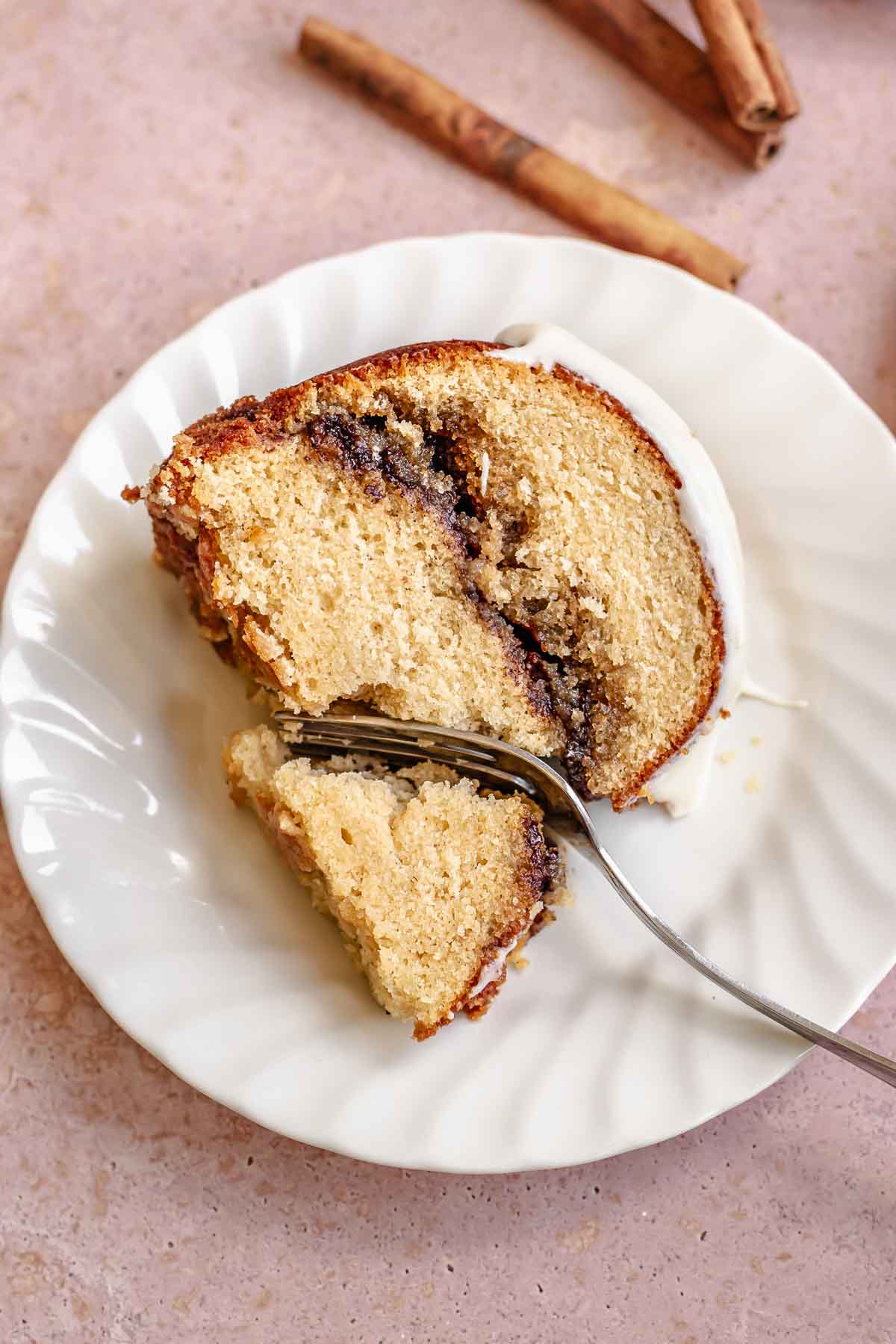 A piece of cinnamon bundt cake on a plate with a fork cutting into it.