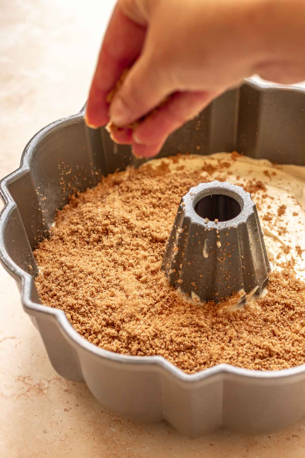 A hand adds cinnamon sugar to the top of the cake batter.
