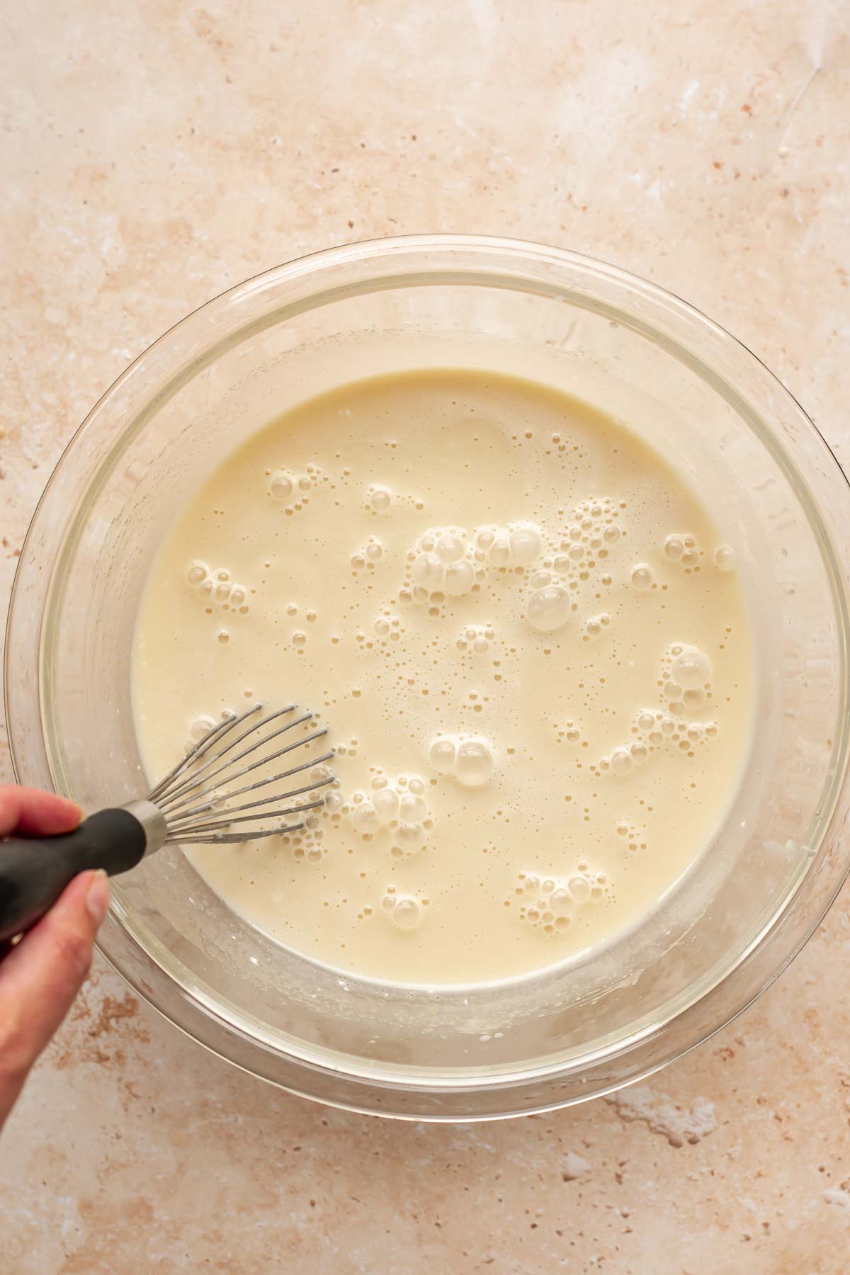 A hand whisks wet muffin batter in a bowl.