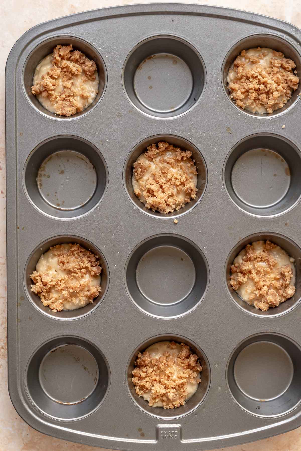 Streusel on top of muffin batter in a muffin tin.