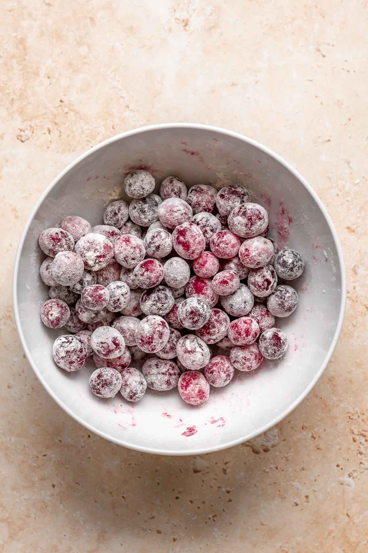 Whole cranberries tossed in a flour in a bowl.