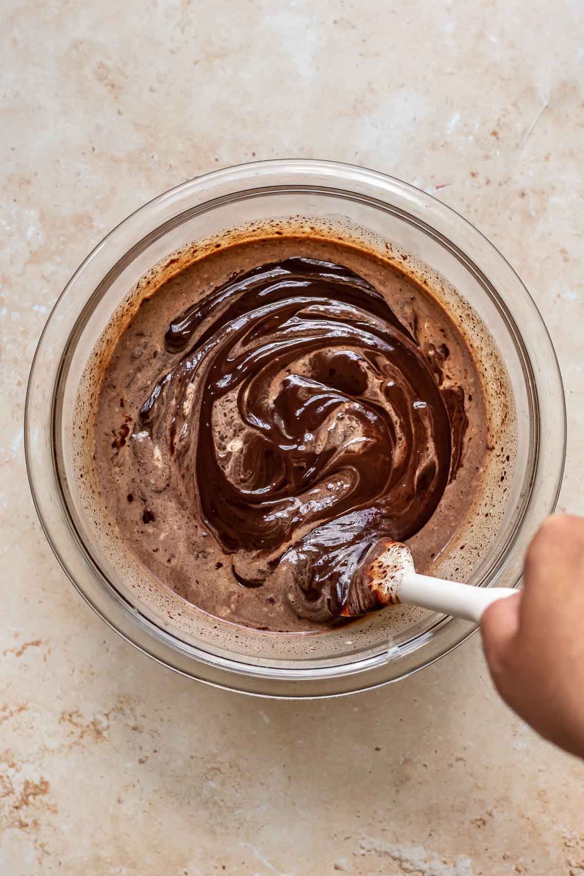 A rubber spatula mixes together dark chocolate ganache in a bowl.