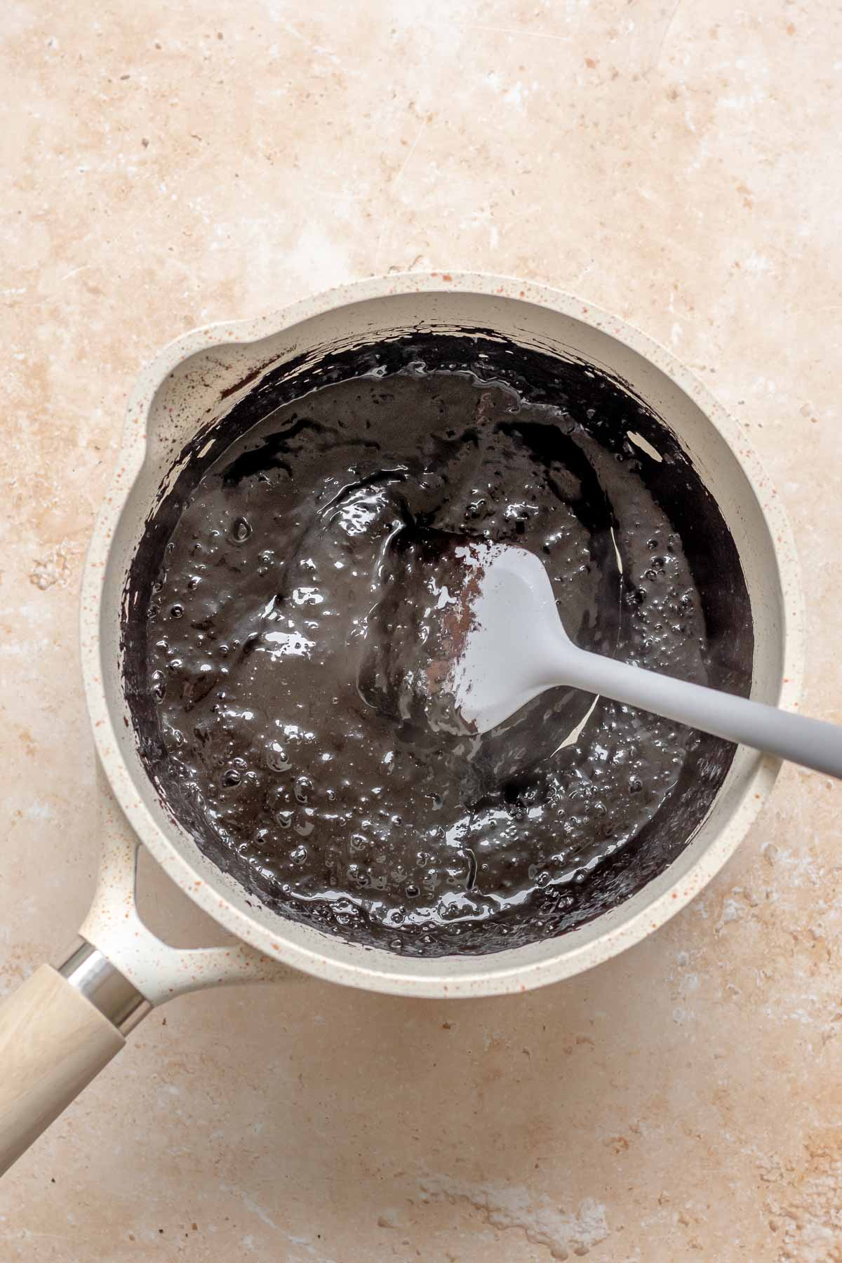 Black cocoa powder, water and cream blooming in a saucepan with a spatula.