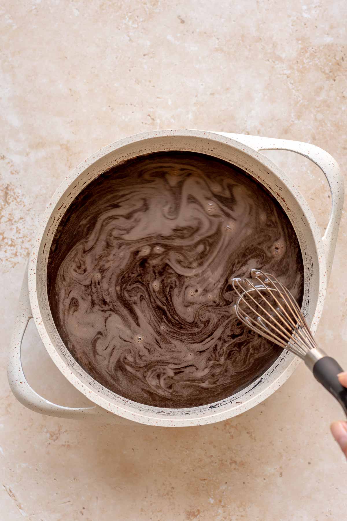 A hand whisks together hot cocoa in a saucepan.